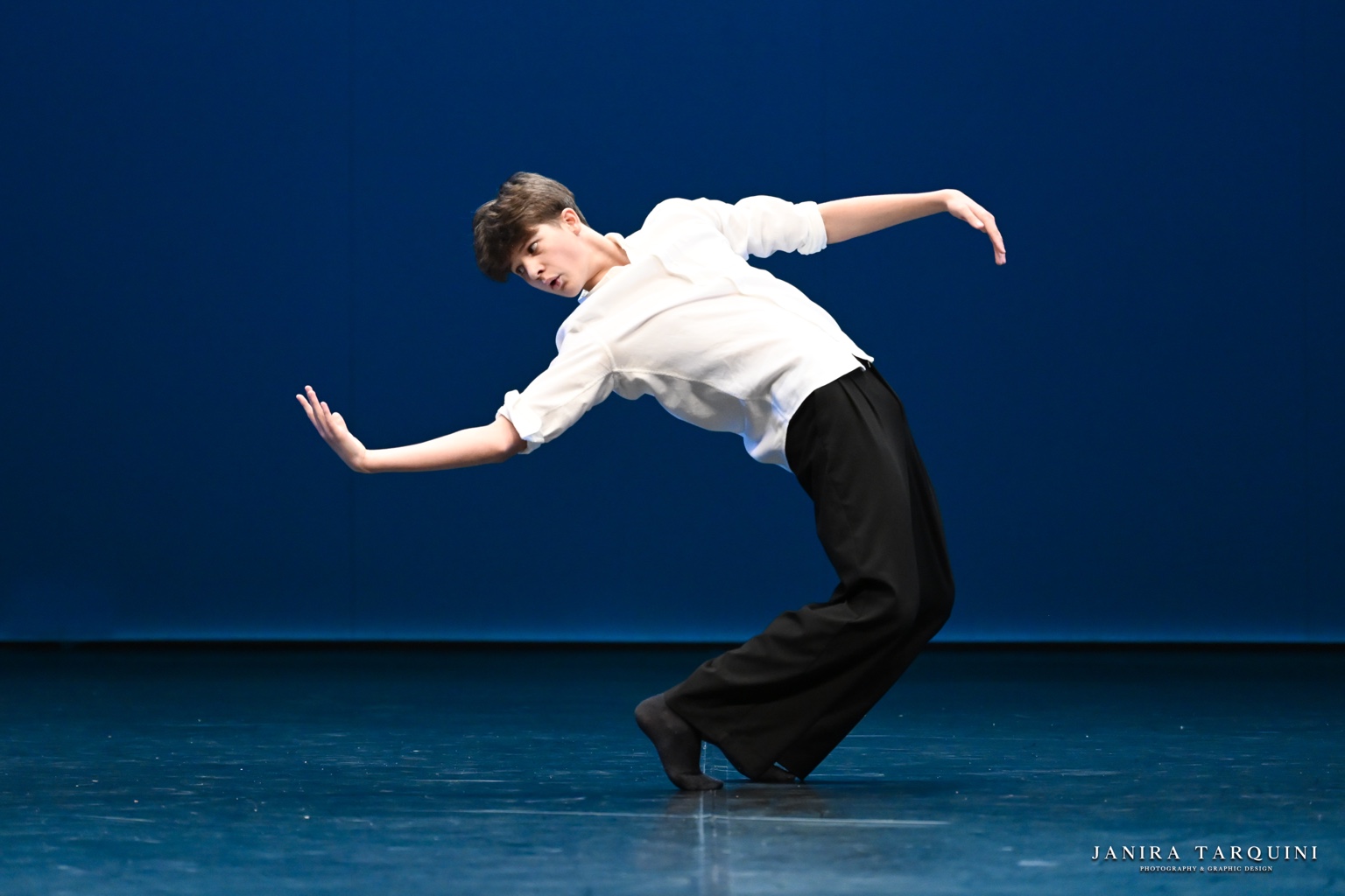 Danzatore in camicia bianca in movimento su un palcoscenico blu